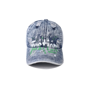 Detail of washed denim baseball cap featuring distressed edges and white artistic graffiti