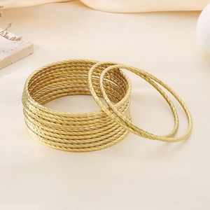 Detailed view of stacked gold twisted cable bangles set on a minimalist warm display