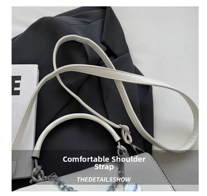 Detailed shot of white leather handbag featuring wide shoulder strap and silver chain