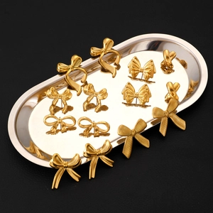 Collection of golden bow-shaped stainless steel earrings on a silver metal tray