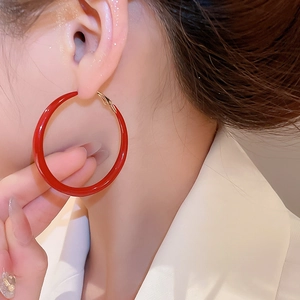 Close-up of model wearing large red enamel hoop earrings with gold metal clasps