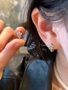 Détail de boucles d'oreilles en argent en forme d'étoile avec zircon bleu portées par un mannequin