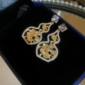Macro shot of gold gourd earrings with filigree rose patterns and sparkling zircons