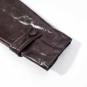 Makroaufnahme von dunkelbraunem PU-Lederärmel mit dekorativem Riemen und Knopfdeteil