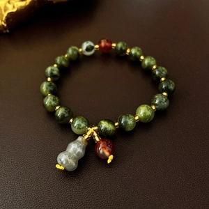 Detail of green ceramic beads bracelet with a white jade gourd charm and gold spacers