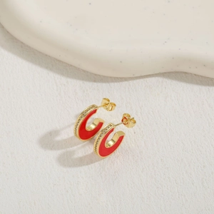 Primo piano degli orecchini a C dorati con smalto rosso e intarsi in zircone bianco