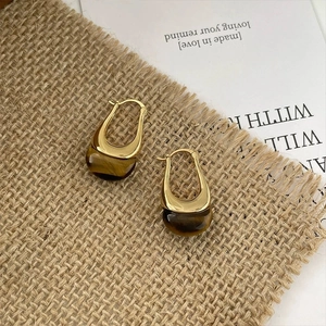 Minimalist gold U-shaped earrings with brown tiger eye stone on a linen background
