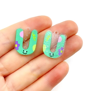 Close-up of mint green U-shaped acrylic charms with cartoon smiley faces and glitter