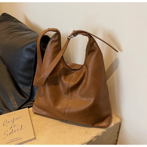 Close-up of brown soft leather hobo bag on a minimalist stone surface with books