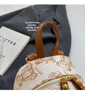 Détail de la poignée en cuir marron et du zip doré sur un mini sac à dos beige