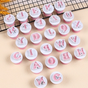High-angle shot of alphabet cookie cutters with pink press handles on a beige surface