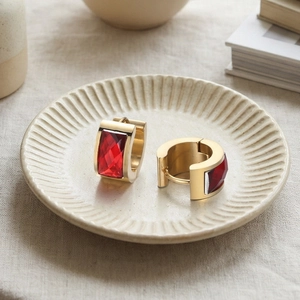 Detail of gold hoop earrings featuring rectangular red faceted gemstone on a ceramic dish