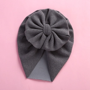 Detailed view of dark grey baby turban hat with a large 3D bow on pink background