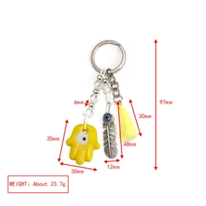 Detailed view of evil eye keychain with hamsa hand, feather charm and yellow silk tassel