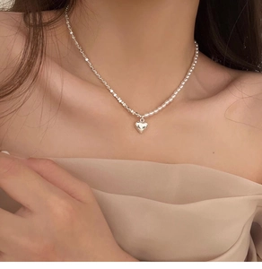 Close-up of a silver heart pendant necklace with pearls on an elegant woman's collarbone
