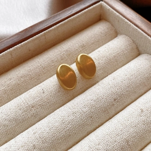 Close-up of golden oval stud earrings with brushed matte finish in a jewelry box