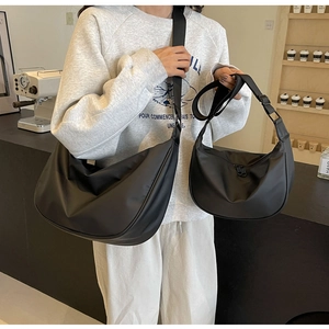 Comparison of black nylon crescent crossbody bags in two sizes worn by a model in a cafe