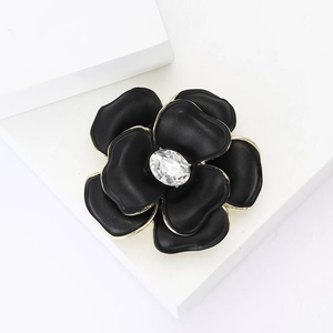 Exquisite black enamel flower brooch with gold edges and crystal center on a white base