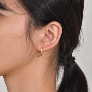 Close-up of minimalist gold U-shaped huggie earrings worn by a model for a modern look
