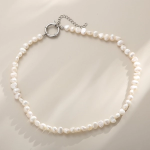 Close-up of baroque freshwater pearl necklace with silver spring clasp on beige surface