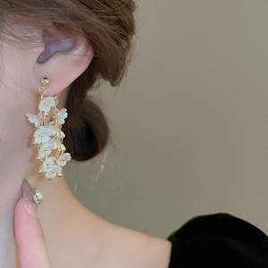 Boucles d'oreilles pendantes fleurs blanches et chaîne dorée portées sur mannequin
