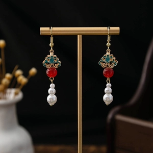 Detail of vintage Chinese earrings with red beads and pearls on a gold display stand