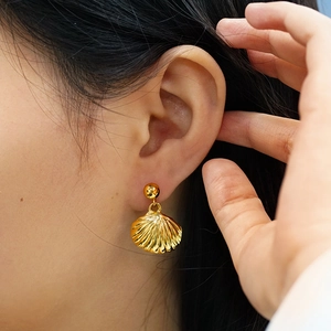 Detail of golden shell drop earrings worn by a model showcasing high polish metallic texture