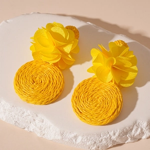 Macro detail of yellow fabric flower earrings with circular woven raffia bohemian charms