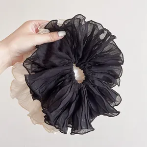 Detail of oversized ruffled chiffon scrunchies in black and beige held in hand