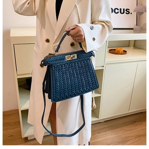 Detail view of navy blue woven trapezoid handbag with gold hardware on a model