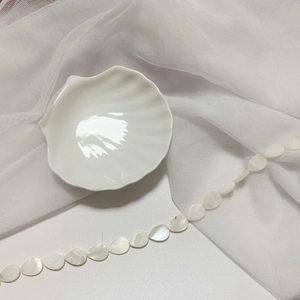 Detail view of drop-shaped mother of pearl beads on a white ceramic shell plate