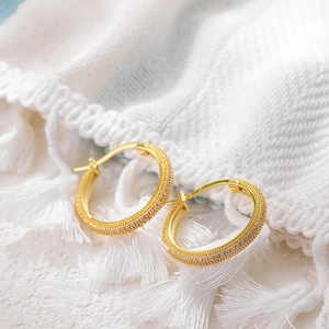 Elegant 18K gold hoop earrings with micro-paved zircons on a soft textured background