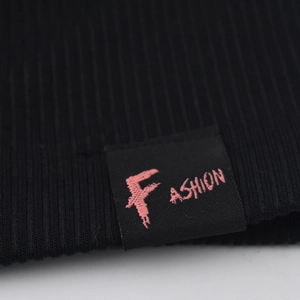 Gros plan du bonnet en tricot noir avec étiquette fashion et lettres roses brodées