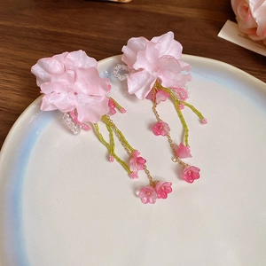 Pink floral tassel earrings with green beads on a white ceramic plate for summer style