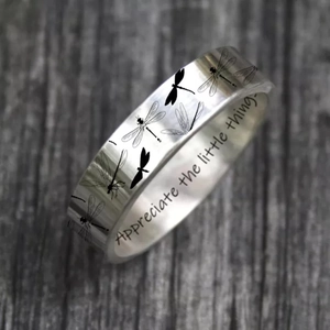 Silver dragonfly ring engraved with Appreciate the little things on grey wood