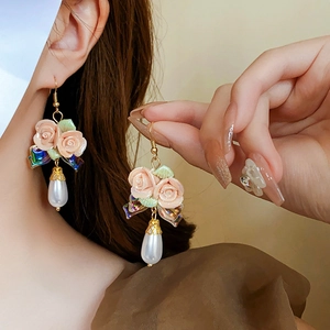 Detail of pink resin flower earring with white pearl drop and gold metallic bow accent
