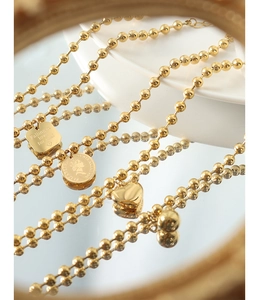 Detailed close-up of gold ball chains with engraved heart and coin charms on mirror