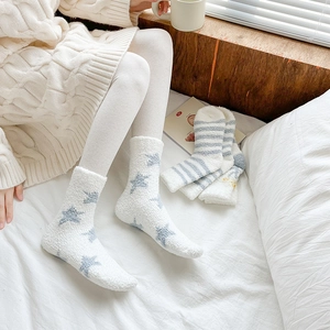 Close-up of soft coral fleece home socks with blue stars on cozy bedroom background