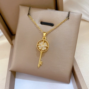 Close-up of golden clover key pendant with white zircon inlays on a dainty cross chain