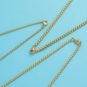 Close-up of golden square box chains with polished metallic finish on blue background