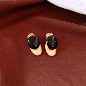 Detail of gold-tone oval earrings with black resin inlay on deep red velvet background