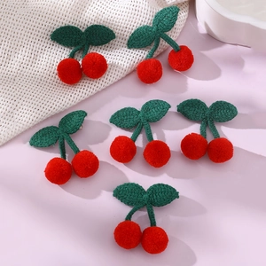 Detailed close-up of six knitted cherry hair clips with red fruits and green leaves