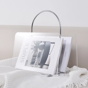 Modern acrylic magazine rack with silver metal frame on a textured white blanket
