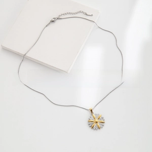 Detail of flower daisy pendant on sleek snake chain necklace with gold and silver tones