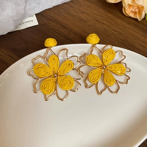 Macro detail of yellow raffia flower earrings with golden beads on a white tray