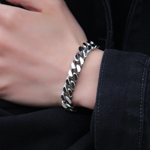 Close-up of a silver stainless steel Cuban link bracelet worn on a wrist over dark clothing