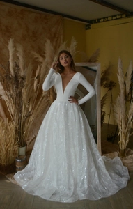 Detailed view of white long-sleeve wedding dress with deep V-neck and sequin lace skirt
