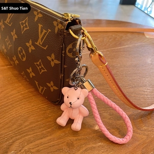 Pink resin bear keychain charm with woven strap attached to a luxury designer handbag