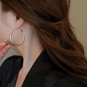 Close-up of minimalist silver oval drop earrings worn by a model for a chic look