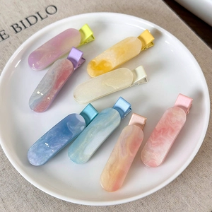 Detailed view of colorful resin hair clips with marble texture on a white ceramic plate